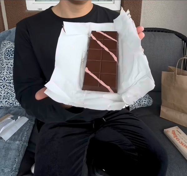 Person holding a chocolate bar with pink drizzle on white wrapper paper