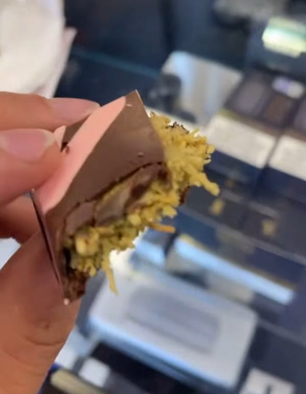 Hand holding a piece of chocolate with kunafeh cover in pistachio cream inside, blurred background