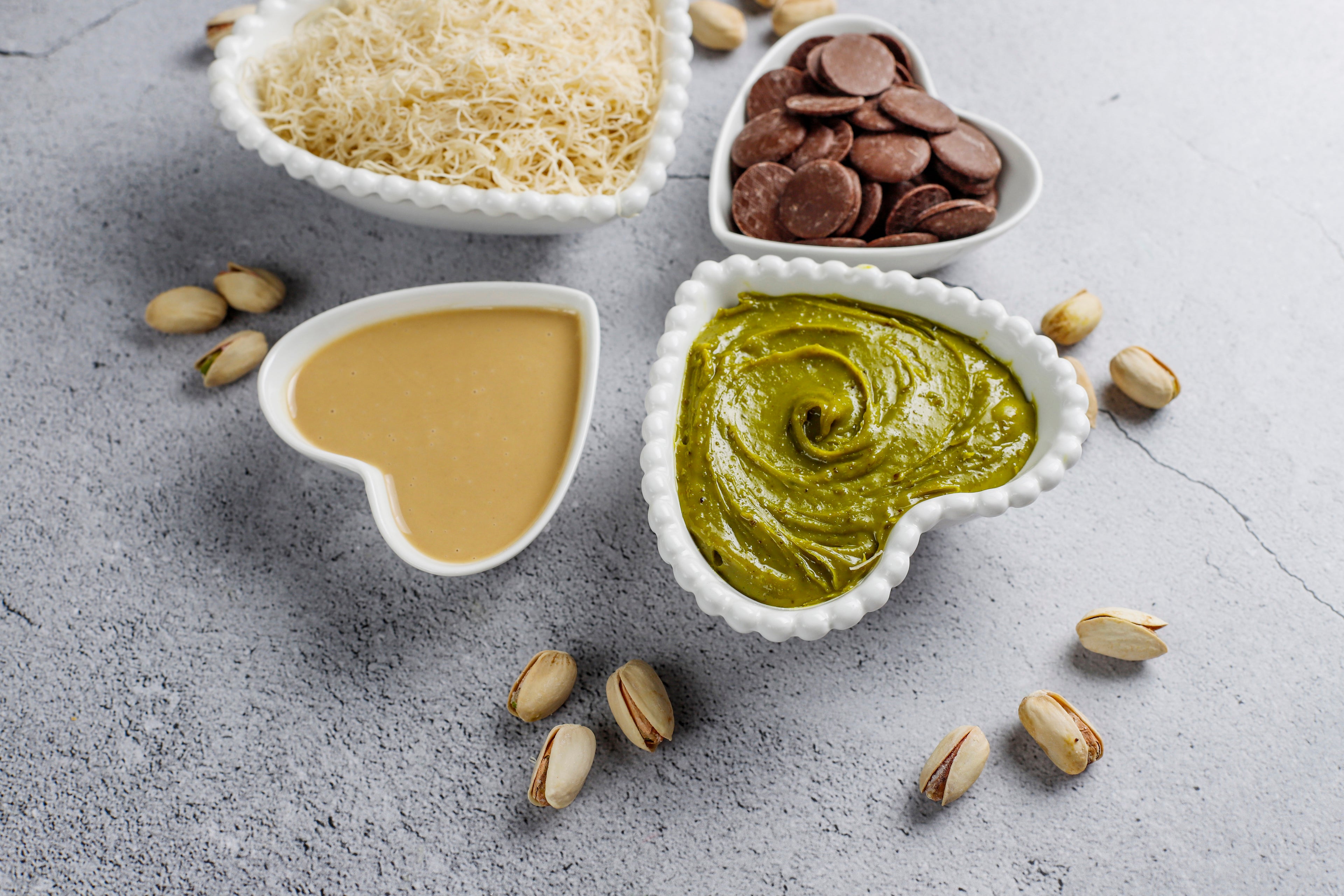 Three heart-shaped bowls with Dubai Chocolate Ingredients on a gray surface.